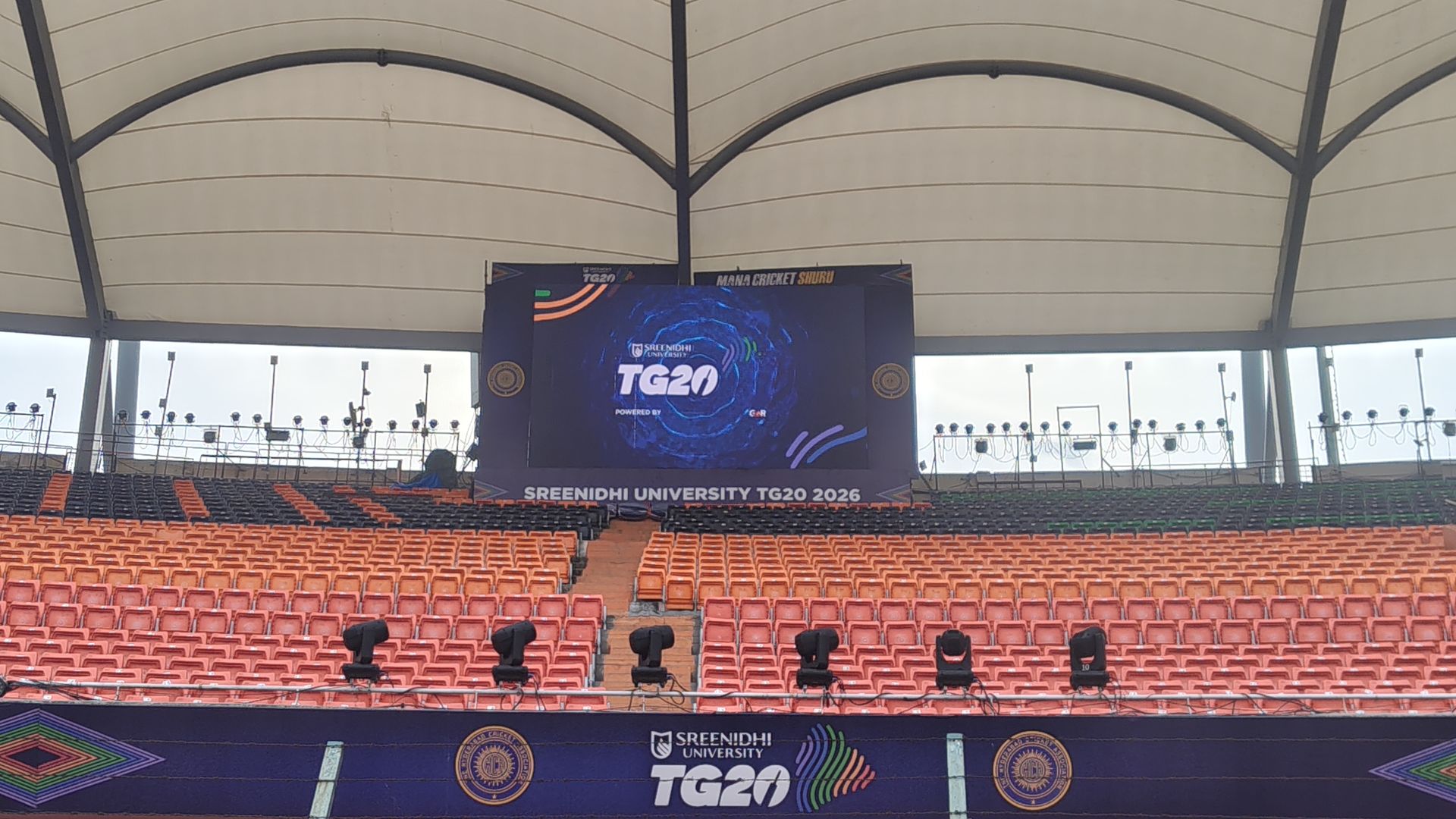 LED video wall rigged inside a covered cricket stadium, showing an event branding screen